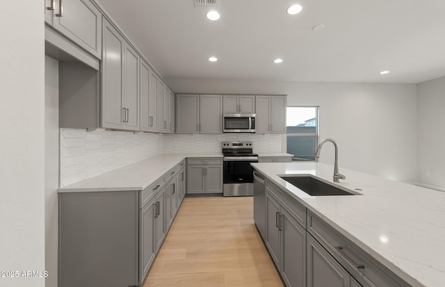 kitchen with gray cabinetry, sink, appliances with stainless steel finishes, light hardwood / wood-style floors, and light stone counters