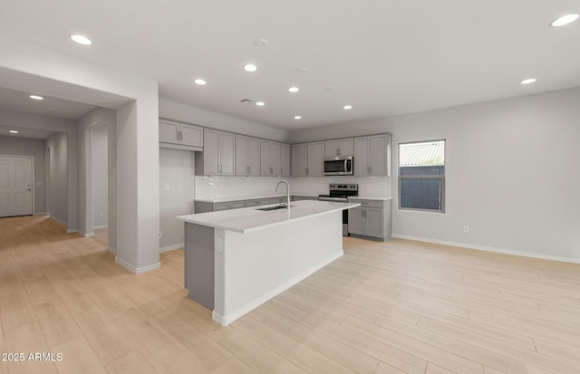 kitchen with a kitchen island with sink, sink, light hardwood / wood-style flooring, gray cabinets, and stainless steel appliances