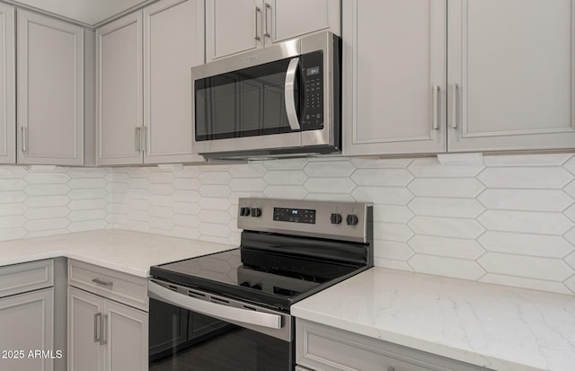 kitchen with decorative backsplash, stainless steel appliances, and light stone counters