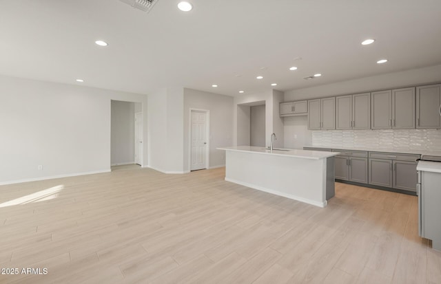 kitchen with sink, light hardwood / wood-style floors, gray cabinets, decorative backsplash, and a center island with sink