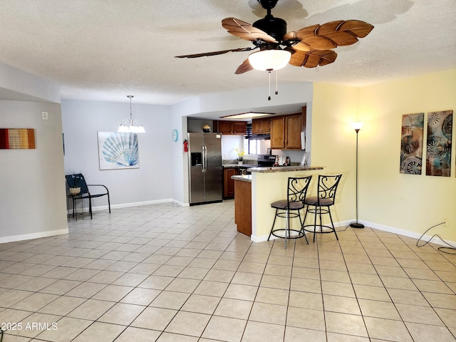 kitchen with light tile patterned flooring, appliances with stainless steel finishes, a breakfast bar, kitchen peninsula, and a textured ceiling