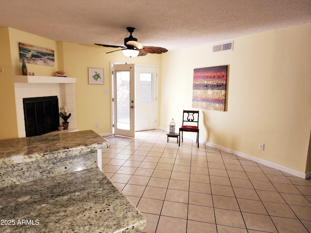 unfurnished living room with a tile fireplace, light tile patterned floors, ceiling fan, a textured ceiling, and french doors