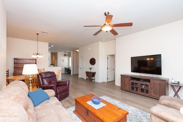 living room featuring ceiling fan with notable chandelier and light hardwood / wood-style flooring