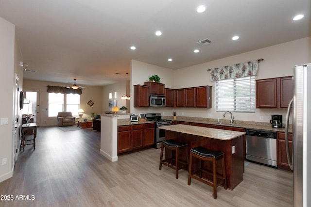 kitchen with a breakfast bar, sink, a center island, light hardwood / wood-style flooring, and appliances with stainless steel finishes