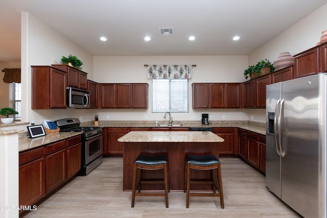 kitchen featuring sink, a kitchen breakfast bar, stainless steel appliances, a center island, and light stone counters