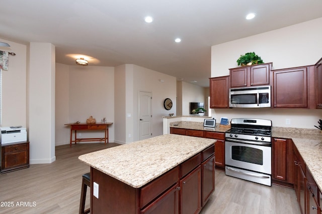 kitchen with stainless steel appliances, a center island, light stone counters, and light hardwood / wood-style floors