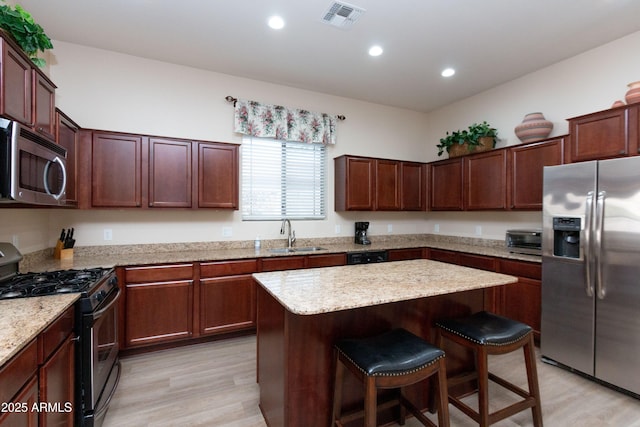 kitchen with sink, a center island, appliances with stainless steel finishes, a kitchen breakfast bar, and light hardwood / wood-style floors