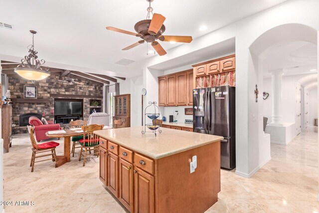 kitchen featuring ceiling fan, a stone fireplace, decorative columns, stainless steel fridge, and light tile patterned flooring