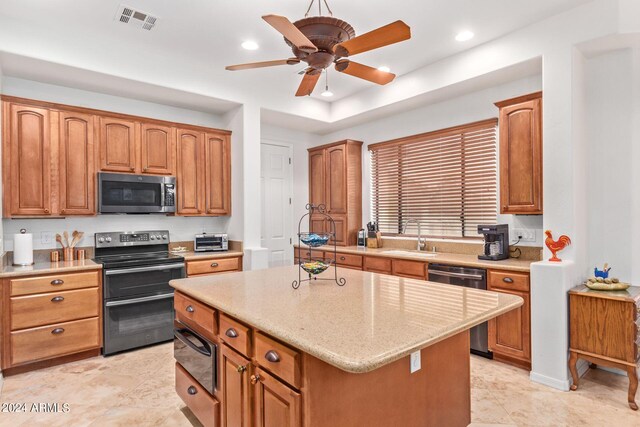 kitchen with stainless steel appliances, sink, light tile patterned floors, a center island, and ceiling fan