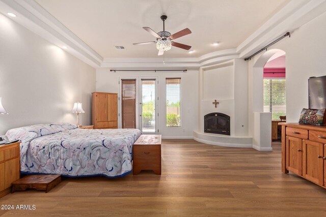 bedroom featuring ceiling fan, access to outside, hardwood / wood-style floors, and a tray ceiling