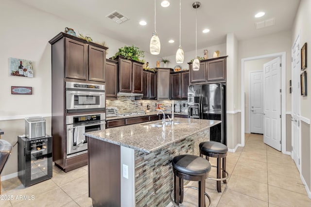 kitchen with visible vents, a sink, stainless steel appliances, light stone countertops, and dark brown cabinets