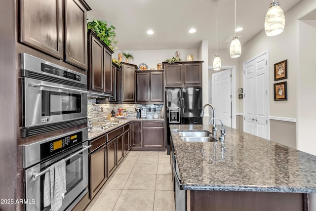 kitchen with dark brown cabinetry, an island with sink, light tile patterned floors, appliances with stainless steel finishes, and a sink