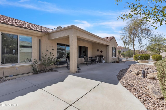 back of house with a tiled roof, a patio area, and stucco siding