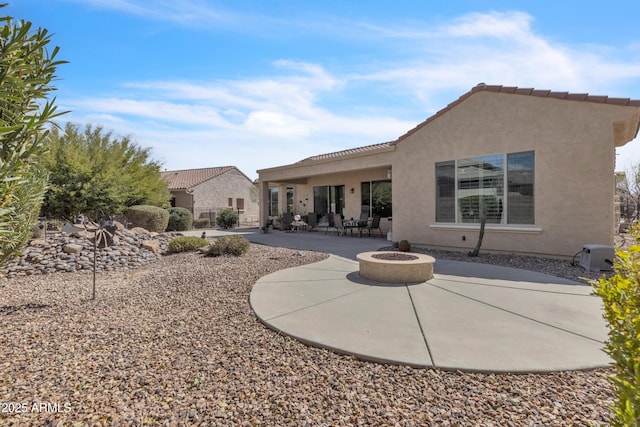 back of house featuring a patio, stucco siding, a tile roof, and an outdoor fire pit