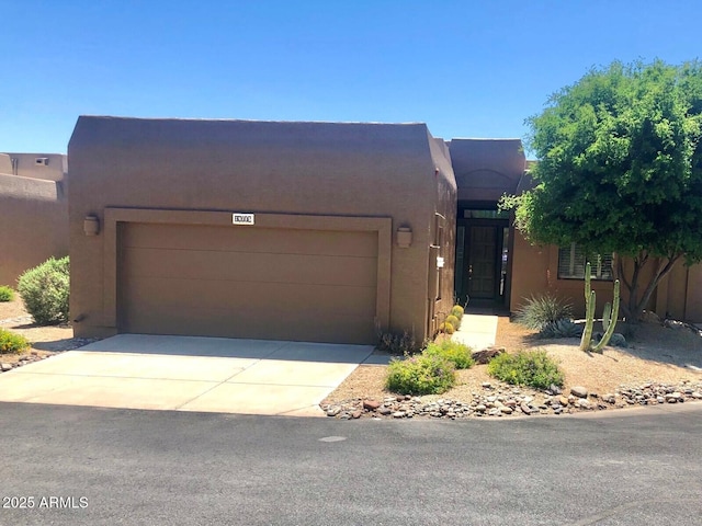 pueblo-style home featuring stucco siding, a garage, and concrete driveway