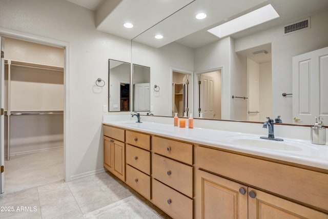 full bathroom with a skylight, double vanity, a walk in closet, tile patterned floors, and baseboards