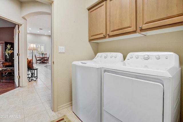 washroom with washing machine and clothes dryer, cabinet space, light tile patterned floors, and arched walkways