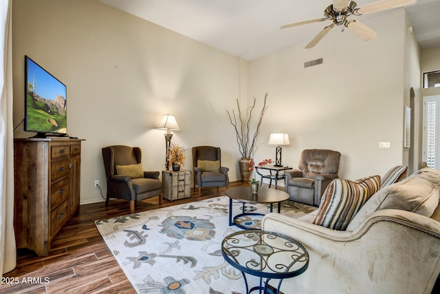 living area featuring wood finished floors, a ceiling fan, baseboards, and a high ceiling