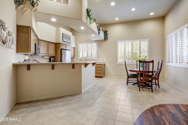 kitchen featuring appliances with stainless steel finishes, a kitchen bar, recessed lighting, brown cabinets, and light countertops