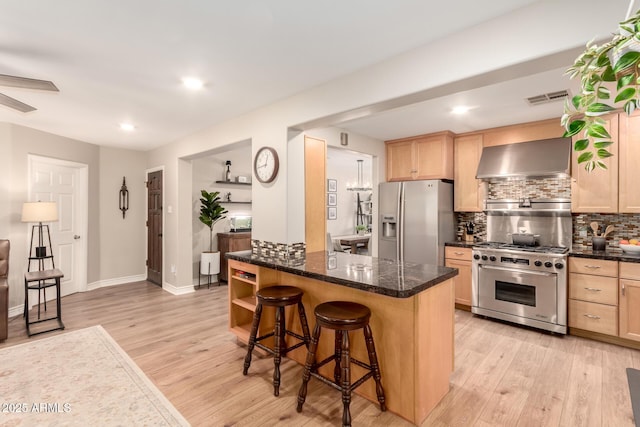 kitchen featuring wall chimney exhaust hood, a kitchen bar, stainless steel appliances, light brown cabinets, and visible vents