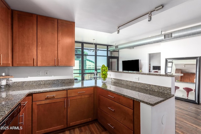 kitchen featuring dishwasher, kitchen peninsula, dark hardwood / wood-style flooring, track lighting, and dark stone counters