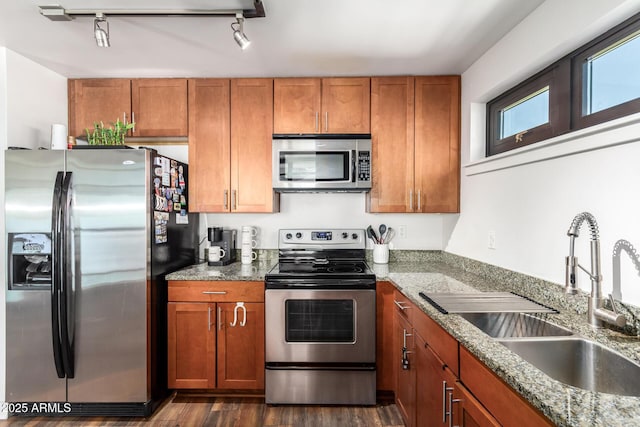 kitchen with stainless steel appliances, dark hardwood / wood-style flooring, track lighting, light stone counters, and sink