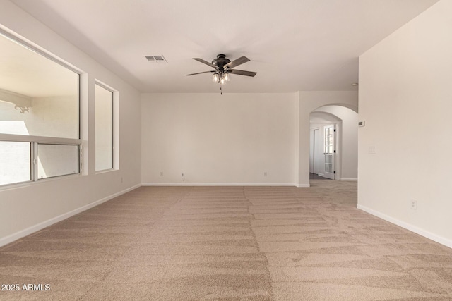 spare room with arched walkways, light colored carpet, visible vents, a ceiling fan, and baseboards