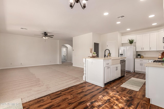 kitchen with arched walkways, a kitchen island with sink, a sink, stainless steel dishwasher, and white fridge with ice dispenser