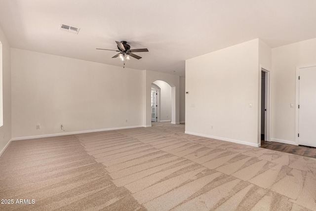 carpeted empty room featuring arched walkways, visible vents, ceiling fan, and baseboards