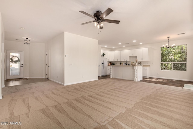 unfurnished living room featuring light carpet, recessed lighting, visible vents, baseboards, and ceiling fan with notable chandelier