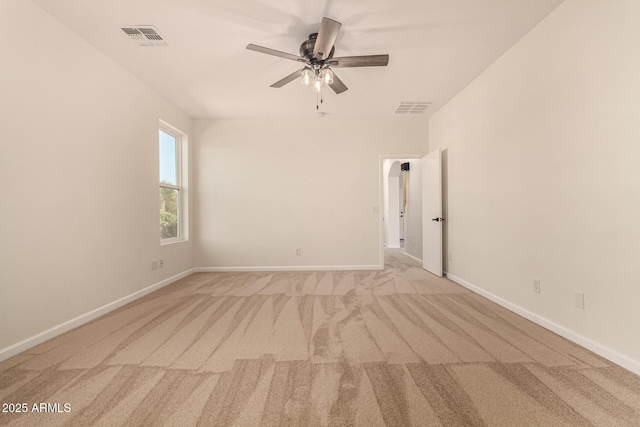 spare room with light colored carpet, visible vents, ceiling fan, and baseboards