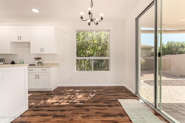 unfurnished dining area with dark wood-style flooring, a notable chandelier, and baseboards