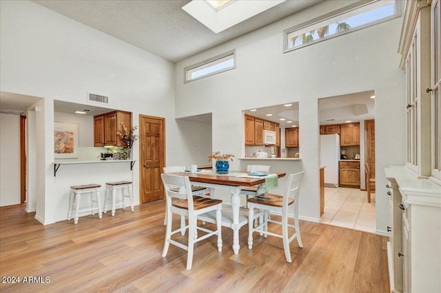 dining area featuring a textured ceiling, a skylight, light hardwood / wood-style floors, and a high ceiling