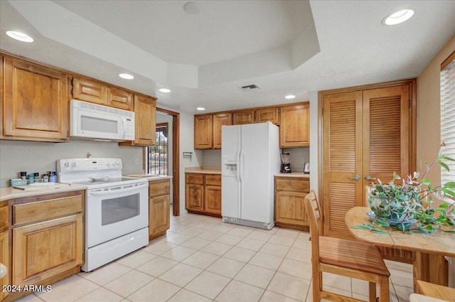 kitchen with light tile patterned flooring, a raised ceiling, and white appliances