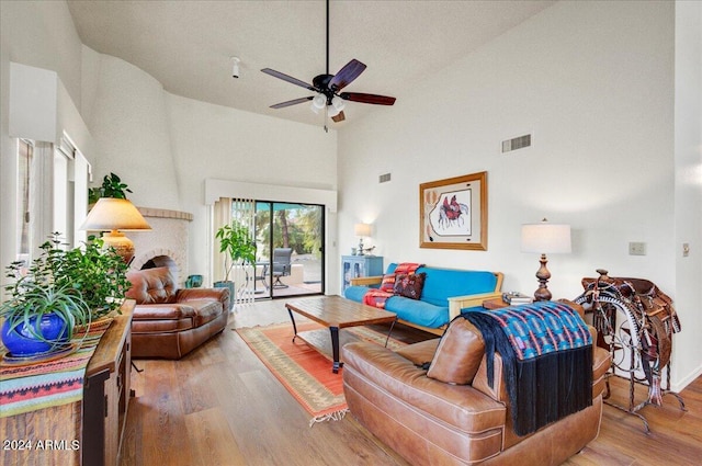 living room with hardwood / wood-style flooring, ceiling fan, high vaulted ceiling, and a brick fireplace