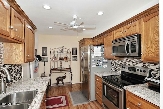 kitchen featuring wood finished floors, a ceiling fan, a sink, appliances with stainless steel finishes, and tasteful backsplash