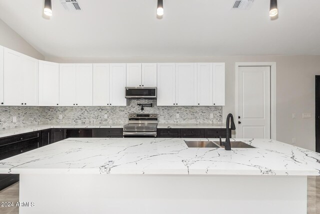 kitchen with light stone countertops, tasteful backsplash, an island with sink, stainless steel appliances, and sink