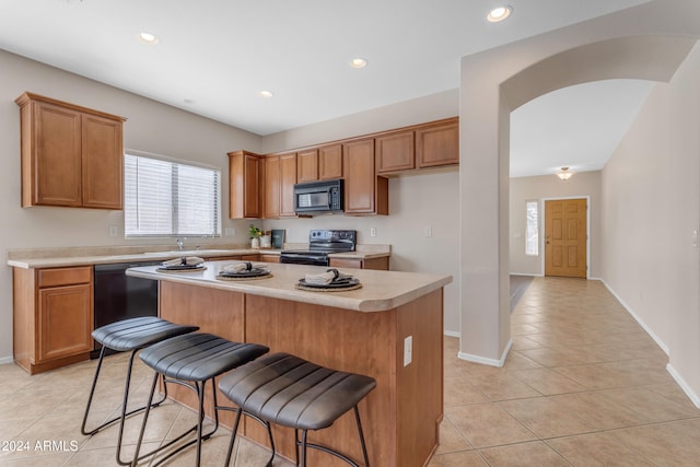 kitchen with a breakfast bar area, a center island, light tile patterned flooring, and black appliances