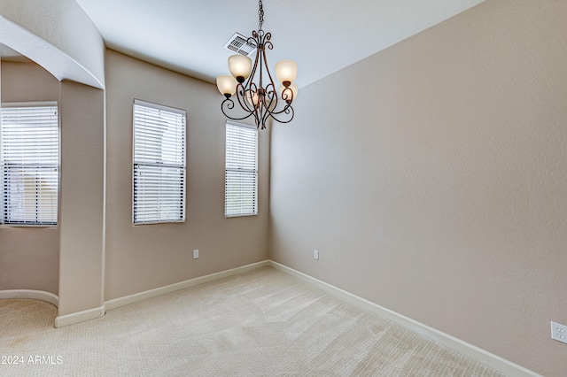 empty room featuring light colored carpet and an inviting chandelier