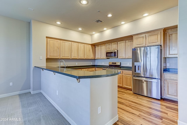 kitchen featuring kitchen peninsula, appliances with stainless steel finishes, light wood-type flooring, and light brown cabinetry