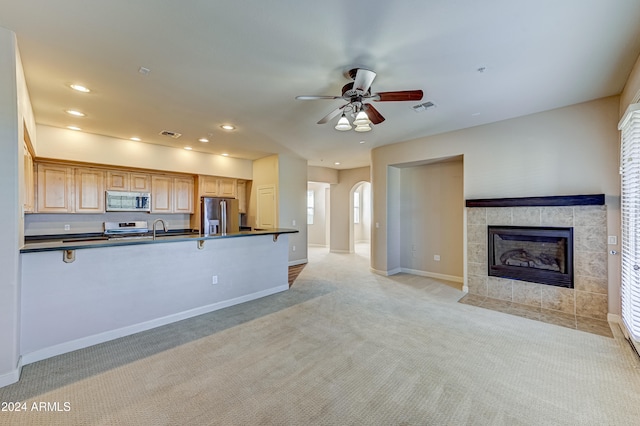 kitchen featuring ceiling fan, a tile fireplace, light carpet, and appliances with stainless steel finishes