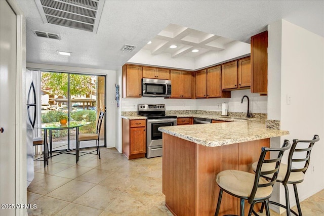 9450 N 94th Pl Unit 106, Scottsdale, AZ 85258 - kitchen with stainless steel appliances, a peninsula, brown cabinetry, a kitchen bar, and a sink