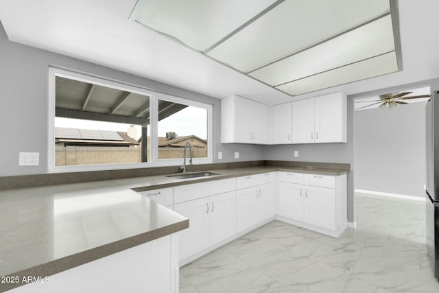 kitchen featuring marble finish floor, dark countertops, white cabinetry, a sink, and baseboards