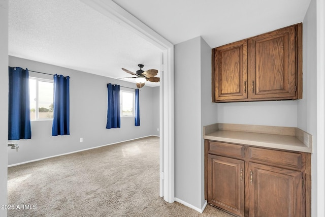 kitchen with light countertops, brown cabinetry, open floor plan, light carpet, and baseboards