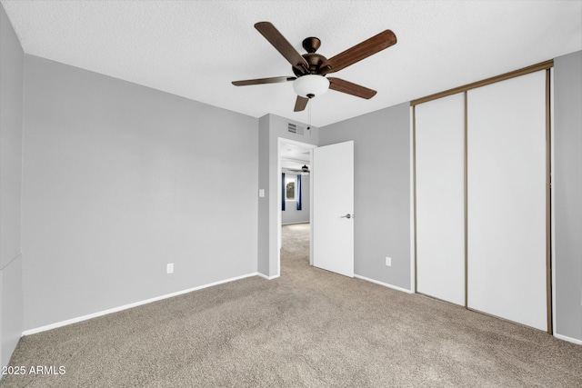 unfurnished bedroom featuring a textured ceiling, ceiling fan, carpet flooring, visible vents, and a closet