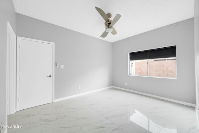 spare room featuring marble finish floor, ceiling fan, and baseboards