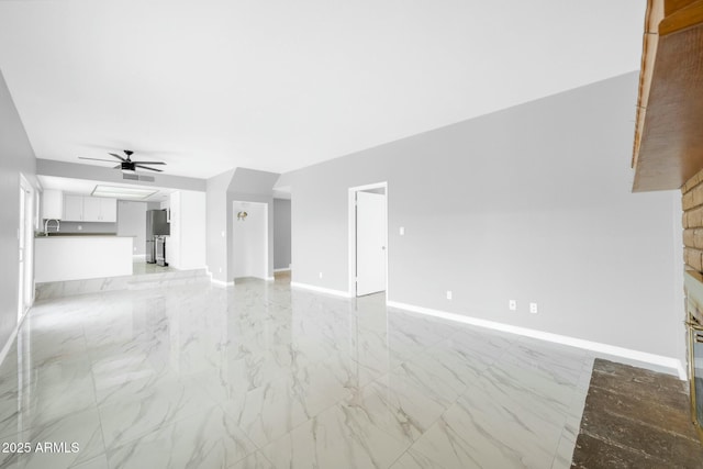 unfurnished living room with ceiling fan, marble finish floor, and baseboards