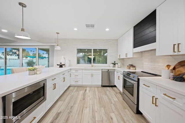 kitchen with hanging light fixtures, stainless steel appliances, white cabinets, and light stone countertops