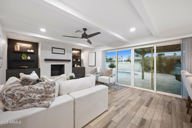 living room with beamed ceiling, ceiling fan, a brick fireplace, and light hardwood / wood-style floors