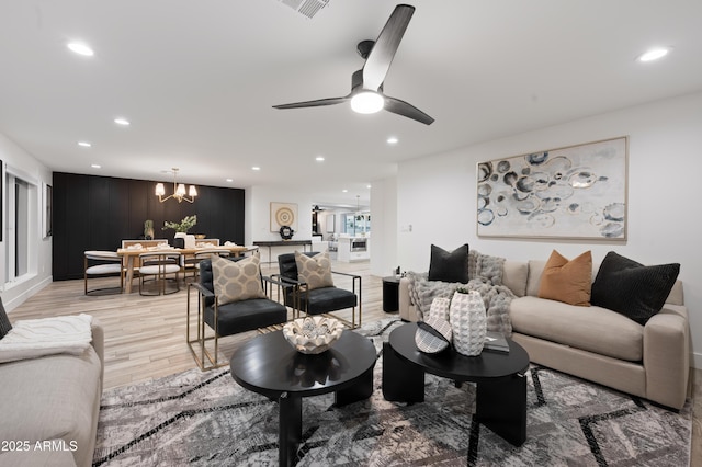 living room with ceiling fan with notable chandelier and light hardwood / wood-style floors